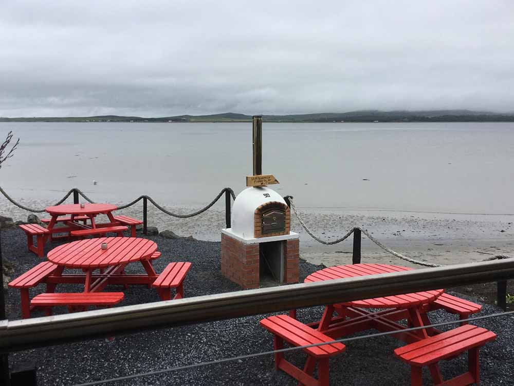 Tables, pizza oven and View of Lochindaal in the outdoor dining area 'The Terrace' at Peatzeria restaurant on Islay