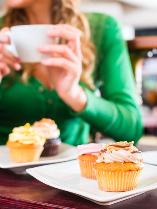 Woman drinking coffee with cupcakes on table