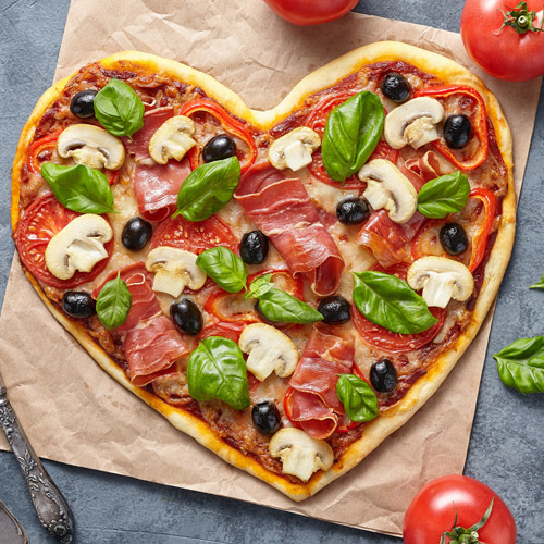 A heart shaped pizza with ham, mushrooms and olives