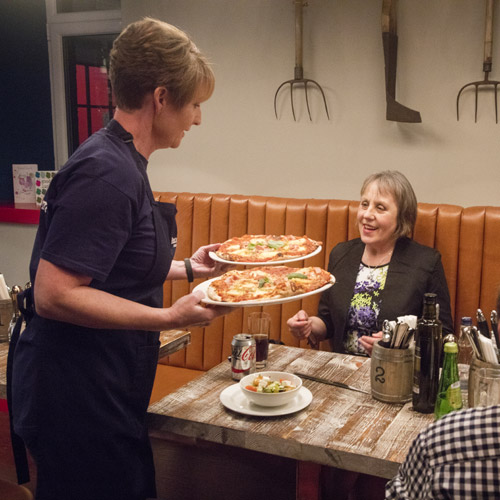 Serving pizzas to customers at table in restaurant