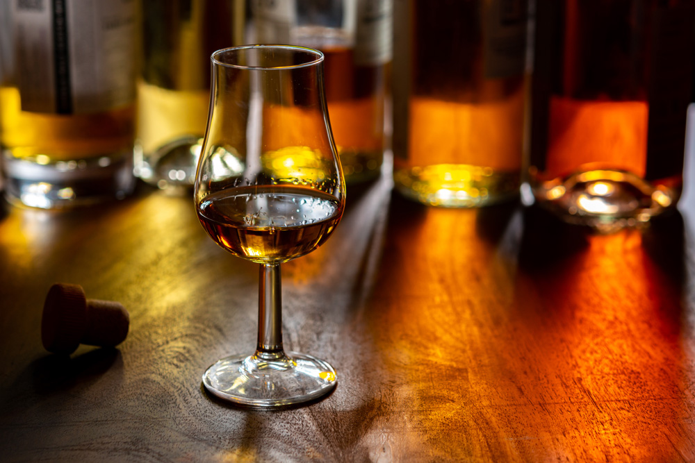 A dram of whisky and a collection of whisky bottles