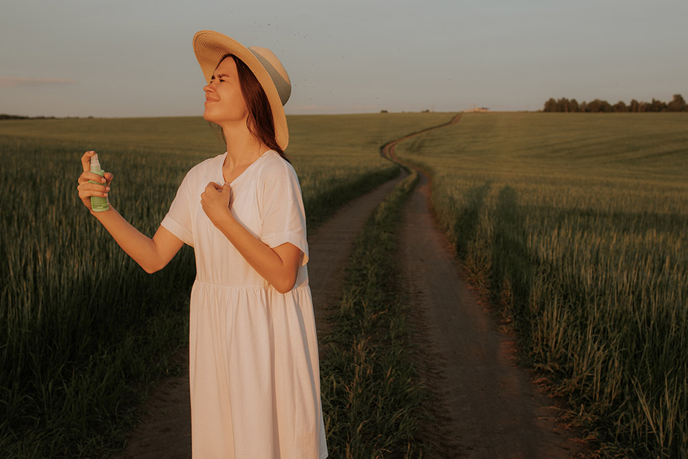 A woman in hat and dress spraying Scottish midge repellant on her face