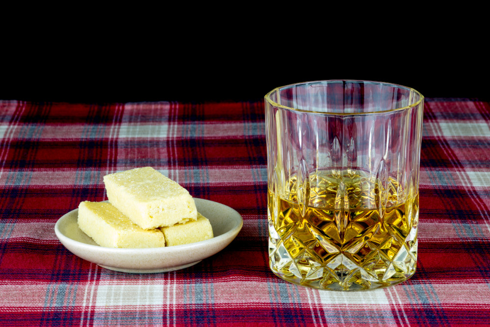 A glass of whisky and plate of shortbread on a tartan tablecloth