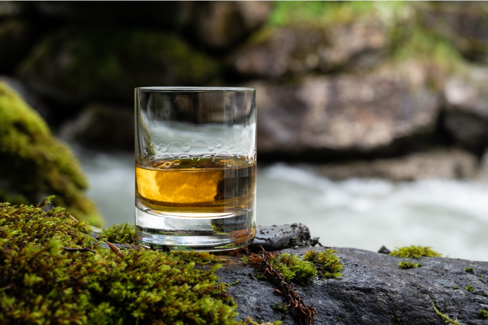Glass of strong scotch single malt whisky with fast flowing mountain river on background, Scotland