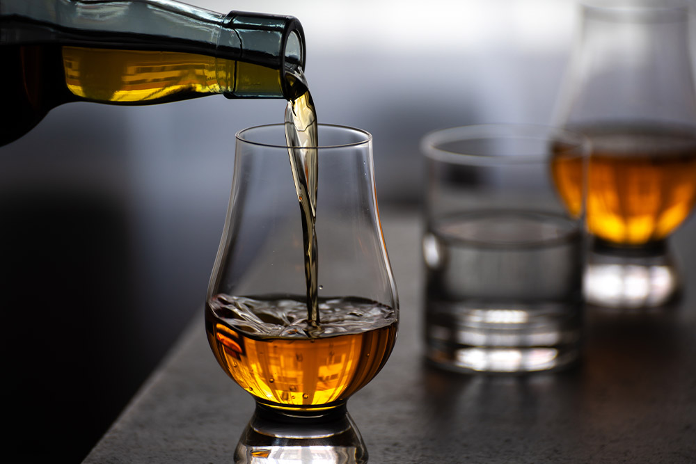 A bottle of whisky is poured into a tulip shaped glass.